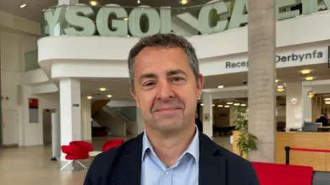 Professor of Endocrinology Aled Rees smiles into the camera at Cardiff University. He is wearing a blue jacket and a blue shirt.